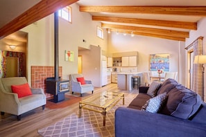 A spacious living area with a sofa, armchairs, a glass coffee table, a fireplace, and a kitchen in the background. - Front St Leavenworth Condo + Parking (Leavenworth)