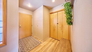 Um corredor com piso de madeira, um tapete estampado, uma porta de madeira e um guarda-roupa de madeira com uma planta verde.