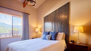 Quarto com uma cama grande, duas luminárias de cabeceira, uma cabeceira de madeira, uma janela com cortinas e vista para o exterior.