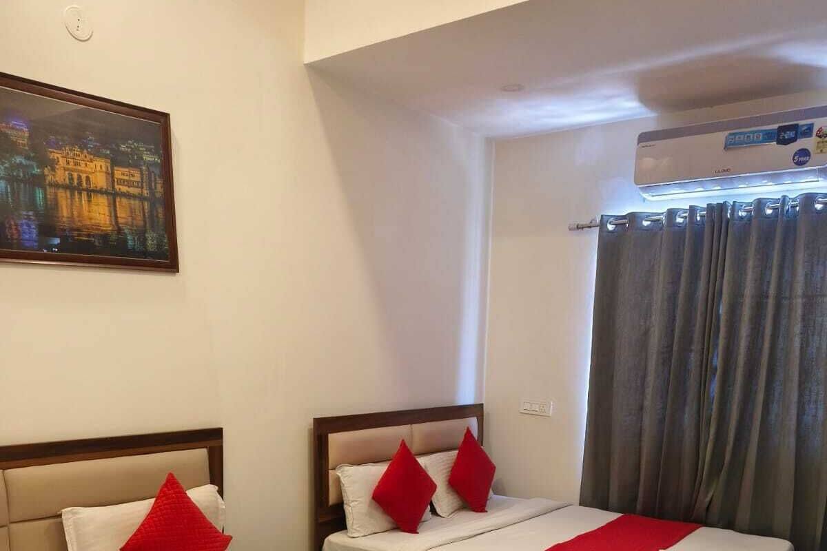 Une chambre d’hôtel avec deux lits, chacun agrémenté d’oreillers rouges et d’une couverture rouge. Un tableau est accroché au mur et un appareil de climatisation est installé au-dessus des lits.