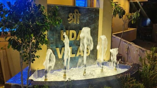 A modern indoor fountain with water jets, surrounded by greenery and a stone wall with the text "KIND VILLAGE". - Hotel Shree Udai Vilas (Udaipur)