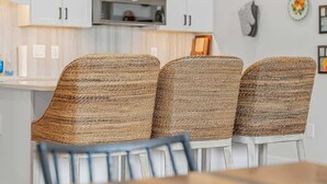 A dining area with three woven chairs and a table, white cabinets, and a microwave above the counter. - Modern Condo Near DT TC | Beach + Bikes (Traverse City)