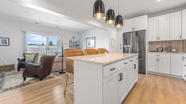 A modern kitchen with white cabinets, a large island, and a stainless steel refrigerator. - Modern Condo Near DT TC | Beach + Bikes (Traverse City)