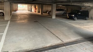 Un parking à plusieurs niveaux, avec des piliers en béton, une rampe et plusieurs voitures garées.