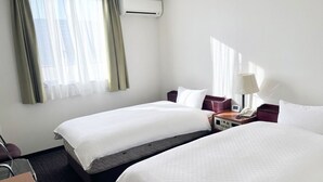 Une chambre d’hôtel avec deux lits, un bureau, une chaise, un appareil de climatisation et une fenêtre avec des rideaux.
