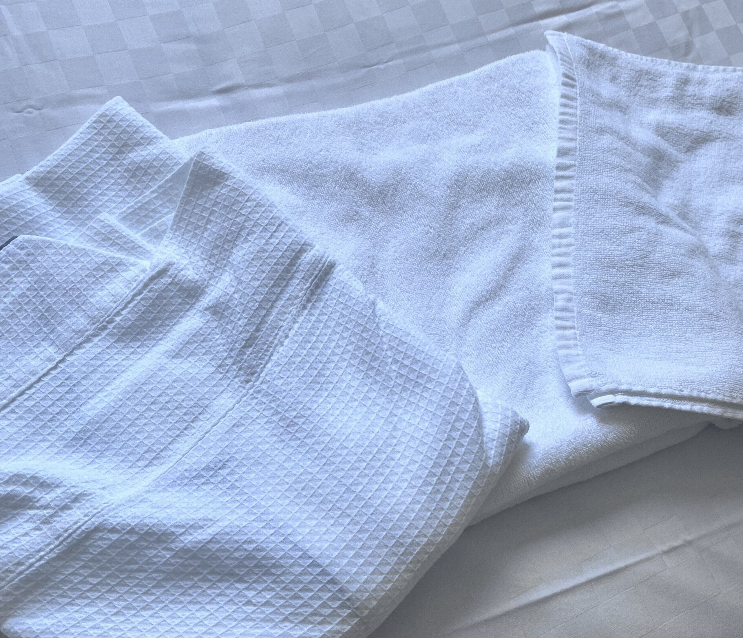 A neatly folded white towel and a white bathrobe on a bed with a checkered pattern.