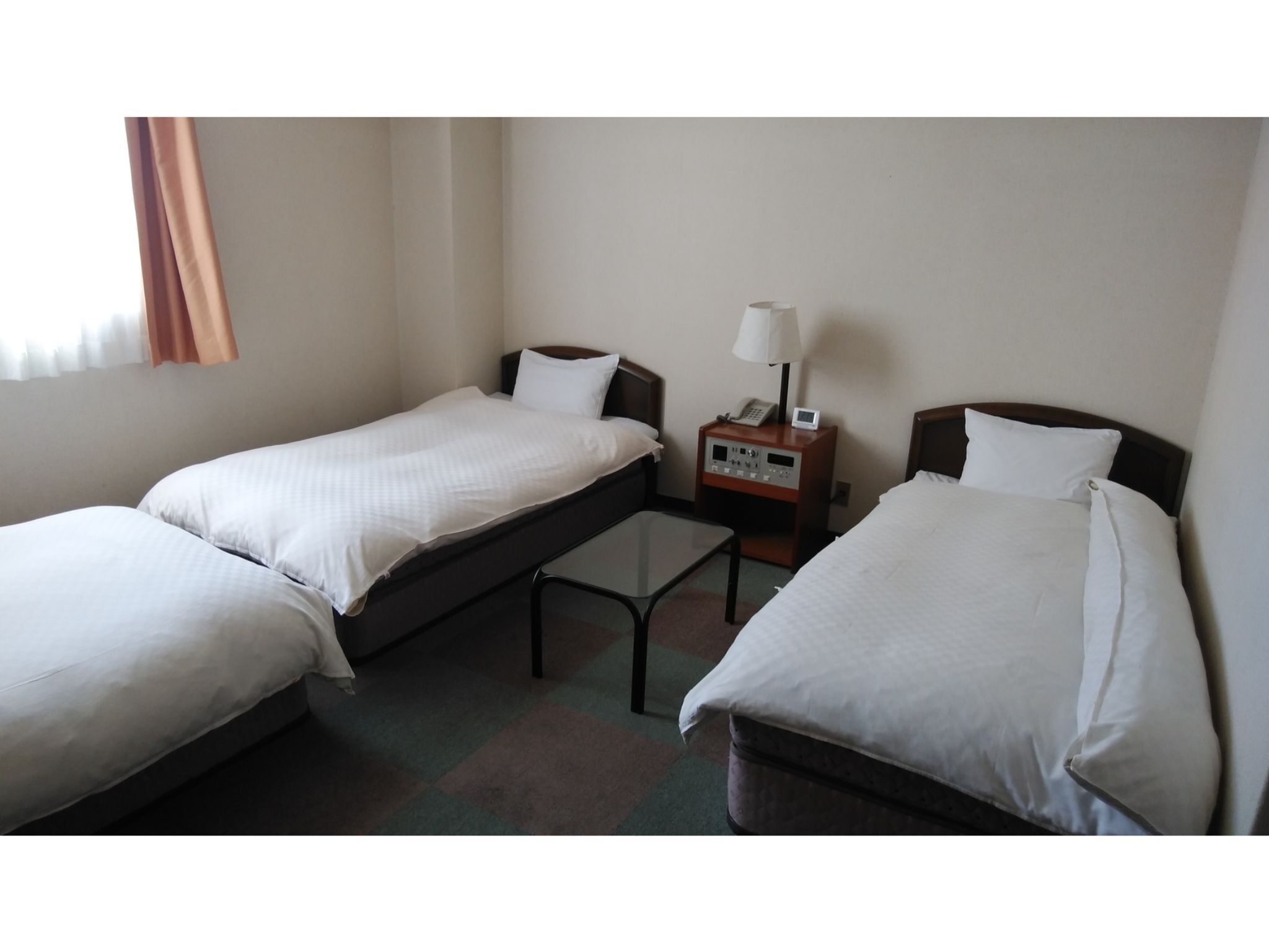 Een hotelkamer met twee enkele bedden, een nachtkastje met een lamp en een klein tafeltje tussen de bedden.