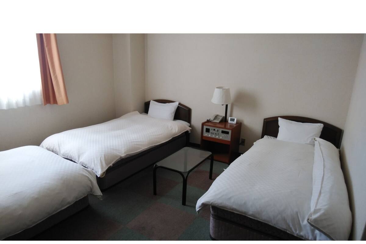Une chambre d’hôtel avec deux lits simples, une table de chevet avec une lampe et une petite table placée entre les lits.