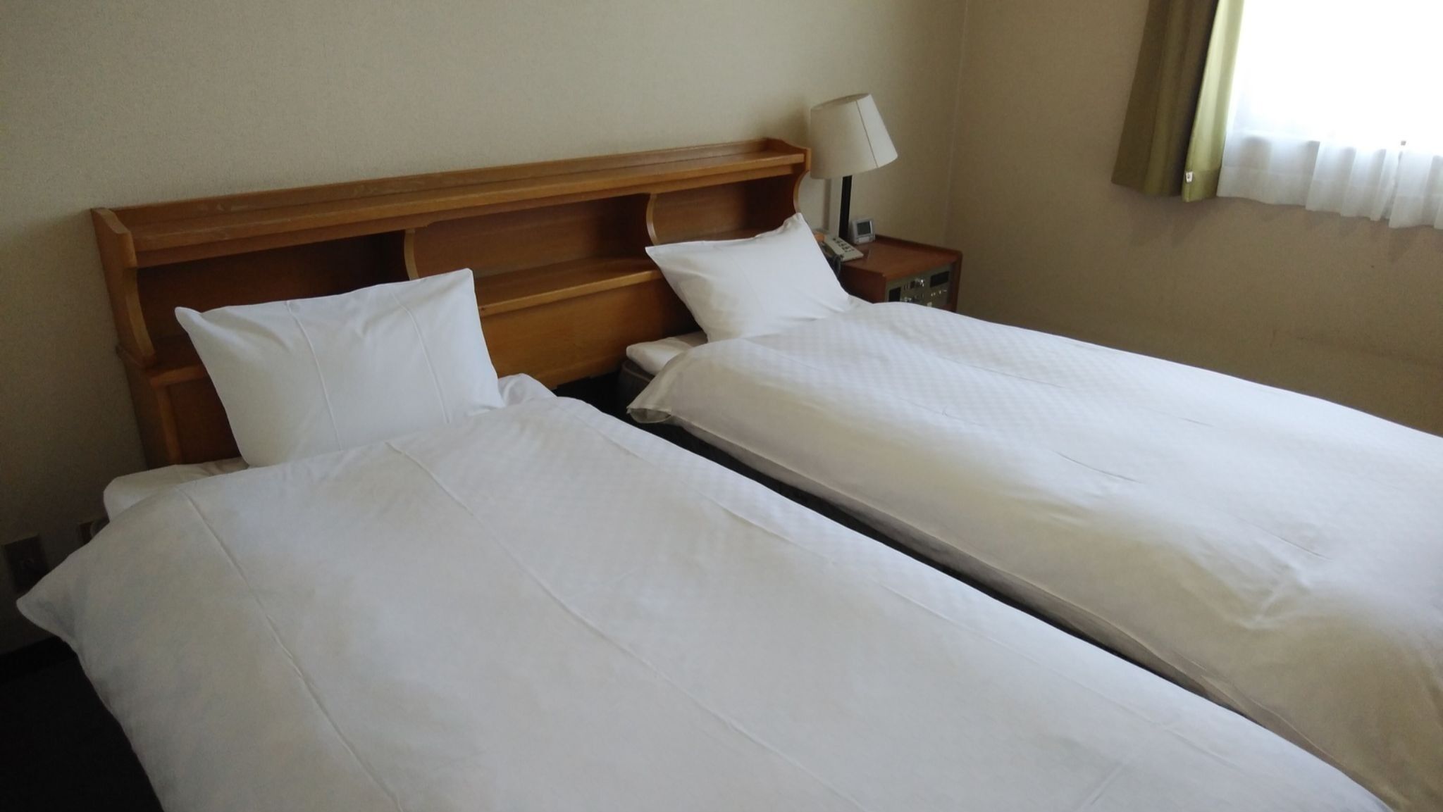 Een hotelkamer met twee eenpersoonsbedden, een houten hoofdbord, een bedlampje en een nachtkastje.