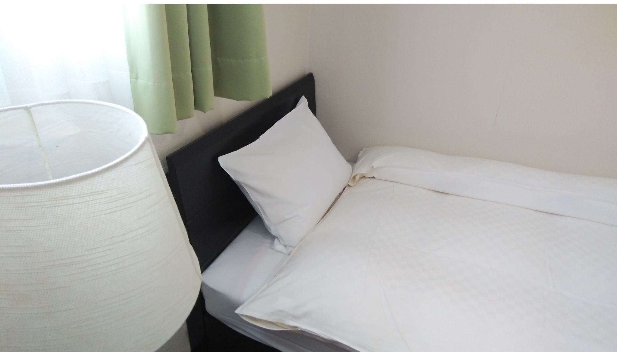Een eenpersoonsbed met witte beddengoed, een zwart hoofdeinde en een witte lamp ernaast.