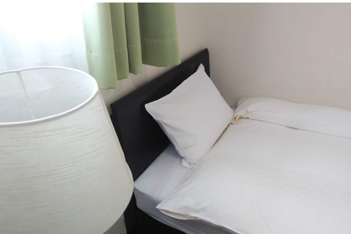 Un lit simple avec une literie blanche, une tête de lit noire et une lampe blanche placée à côté.