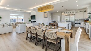 Une cuisine spacieuse équipée d’appareils modernes, un coin repas avec des chaises en osier et un salon avec un canapé et une télévision.