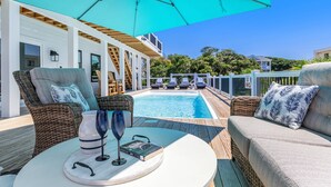 Un espace aménagé au bord de la piscine, avec des meubles en osier, un parasol turquoise et une vue sur la piscine et la végétation environnante.