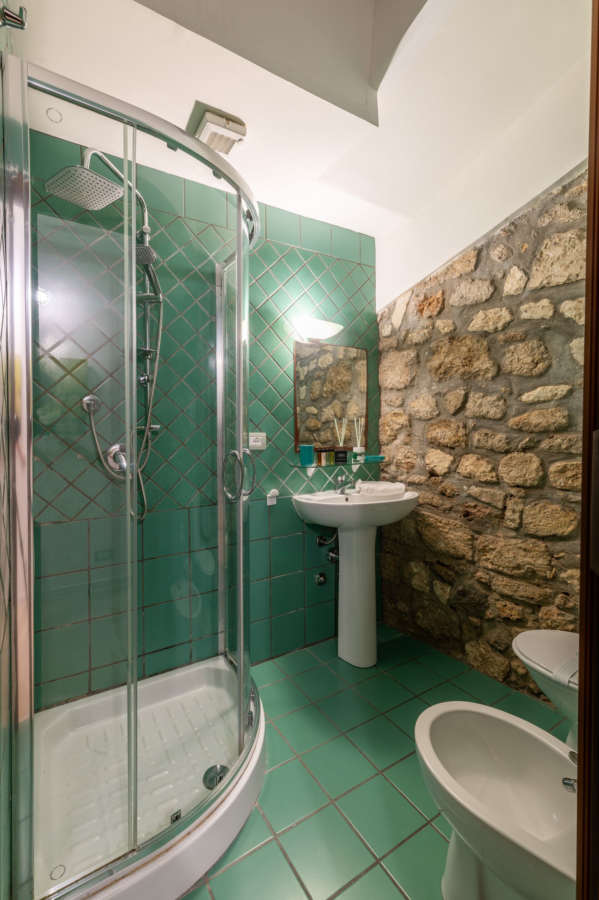 A bathroom with a glass-enclosed shower, a pedestal sink, and a stone wall.