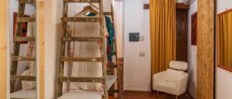A compact room with a wooden ceiling, a bed with an orange blanket, a white chair, a wooden ladder, and a television.