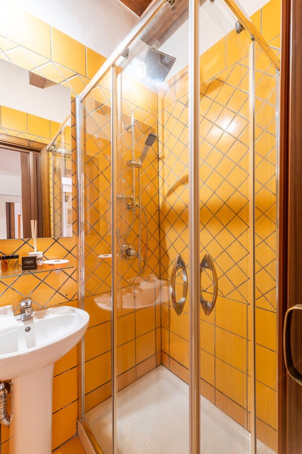 A modern bathroom with a glass-enclosed shower, a white sink, and yellow-tiled walls.