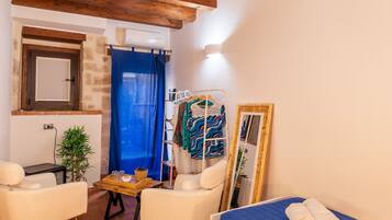 Una habitación pequeña y acogedora con cama, dos sillones, una mesa, un espejo y una lámpara colgante.