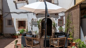 Un patio con mesas al aire libre, un edificio blanco con detalles de piedra y plantas en macetas.