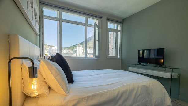 Una habitación de hotel con cama, televisor y ventana con vista a edificios y una colina.