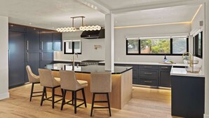 A modern kitchen with a central island, dark cabinetry, and a large window providing a view of the outdoors.