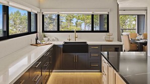 A modern kitchen with dark cabinetry, a black countertop, and a large window offering a view of trees.
