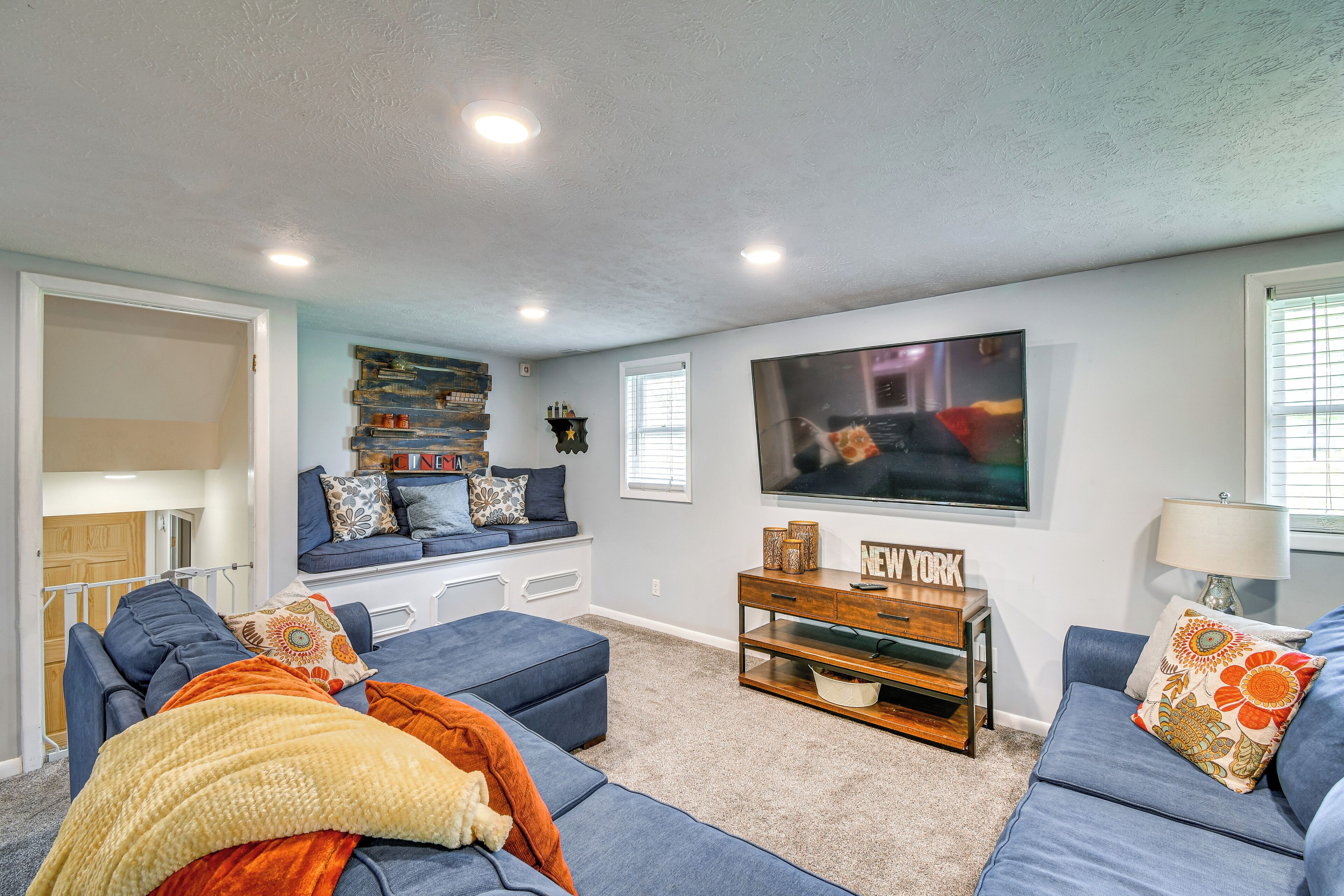 A modern living room with a large flat-screen TV, blue sofas, and a wooden entertainment unit.