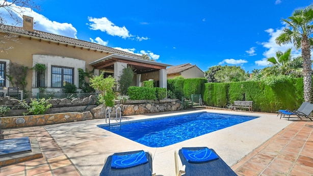 A swimming pool with two lounge chairs, a stone wall, and a covered patio area. - Alondra - Javea, Costa Blanca (Javea)