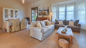 A spacious living room with a beige sofa, a wooden coffee table, and a dining area with a table and chairs. - Alondra - Javea, Costa Blanca (Javea)