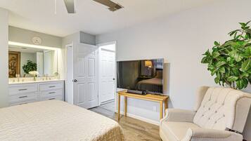Un dormitorio con una cama, un televisor sobre una mesa de madera, una silla y una puerta que da a otra habitación.