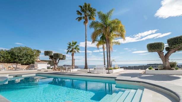 Ein Swimmingpool mit klarem, blauem Wasser, umgeben von Liegestühlen und Palmen.