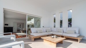 Ein modernes Wohnzimmer mit einem Ecksofa, einem Holztisch und einer Glastür zu einem weiteren Raum.