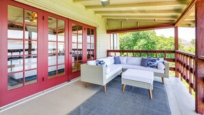 Eine überdachte Veranda mit einem weißen Sofa, einem Hocker, Glastüren mit roten Rahmen und einem Deckenventilator.