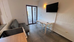 Un espacio habitable moderno con un sofá, una mesa de comedor con sillas, un televisor montado en la pared y un ventanal corredizo que da a un área exterior.