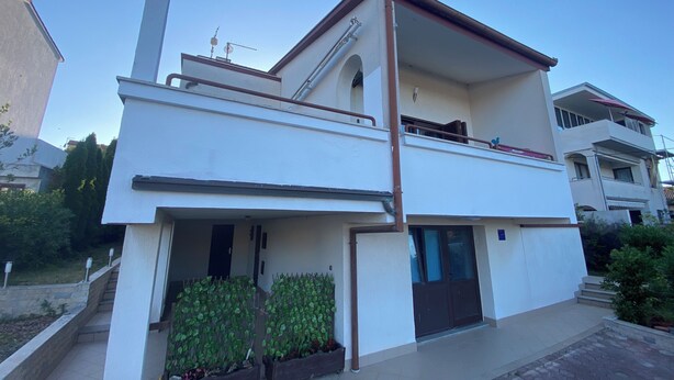 Un edificio residencial de dos pisos con techo plano, un balcón en el nivel superior y una entrada principal con puerta y ventanas.