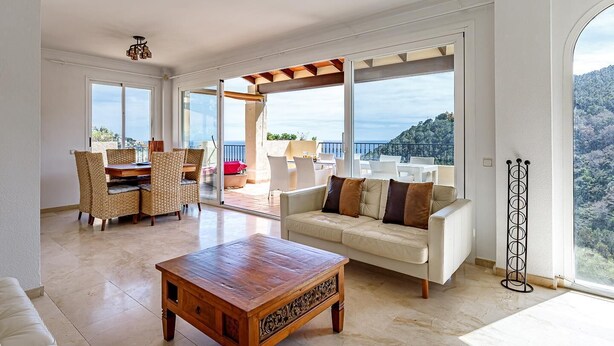 A spacious living room with a wooden coffee table, a beige sofa with brown cushions, wicker chairs, and a balcony with a view of the sea. - Altea Buganvillas - Altea, Costa Blanca (Altea)