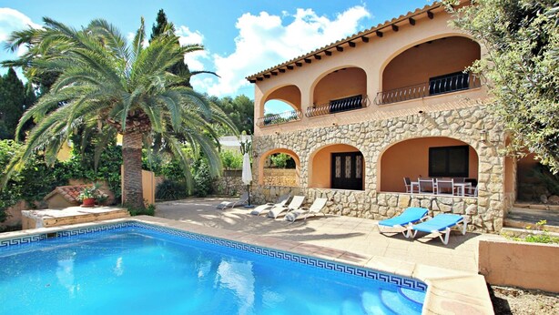 A poolside area with a stone building, palm trees, and lounge chairs.