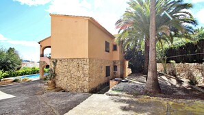 A two-story building with a stone base and a beige upper level, surrounded by palm trees and a pool.