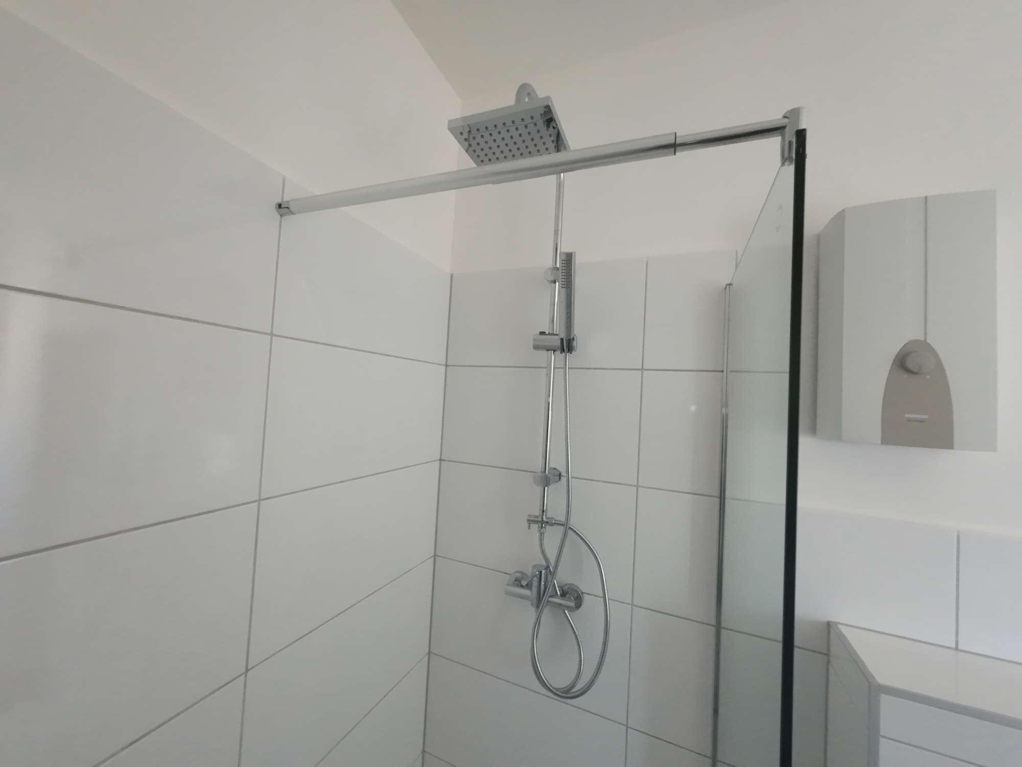 Une douche moderne dotée d’un pommeau de douche à main, d’un pommeau de douche fixe et d’une cabine de douche en verre.