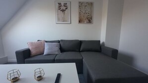 A modern living room with a grey sectional sofa, two cushions, a white coffee table, and two wall-mounted artworks. - Light-filled 100 m², 5-Room Holiday Apartment with Space, Style & Comfort (Solingen)