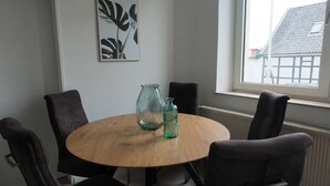 Ett runt träbord med fyra mörka stolar, två glasflaskor och ett inramat konstverk på väggen.