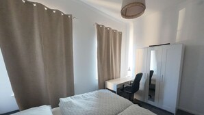A hotel room with two beds, a desk, a chair, a wardrobe, and a hanging light fixture. - Duplex apartment with two bedrooms and a living room (Solingen)