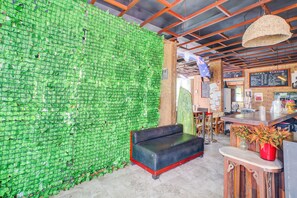 A bar area with a green bottle wall, a black leather sofa, and a wooden counter. - Collection O Bali near Sanur Beach formerly Akarsa Kokoro (Denpasar)