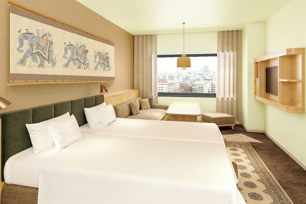 A hotel room with a large bed, a sofa, a small table, a TV, a painting, and a city view.