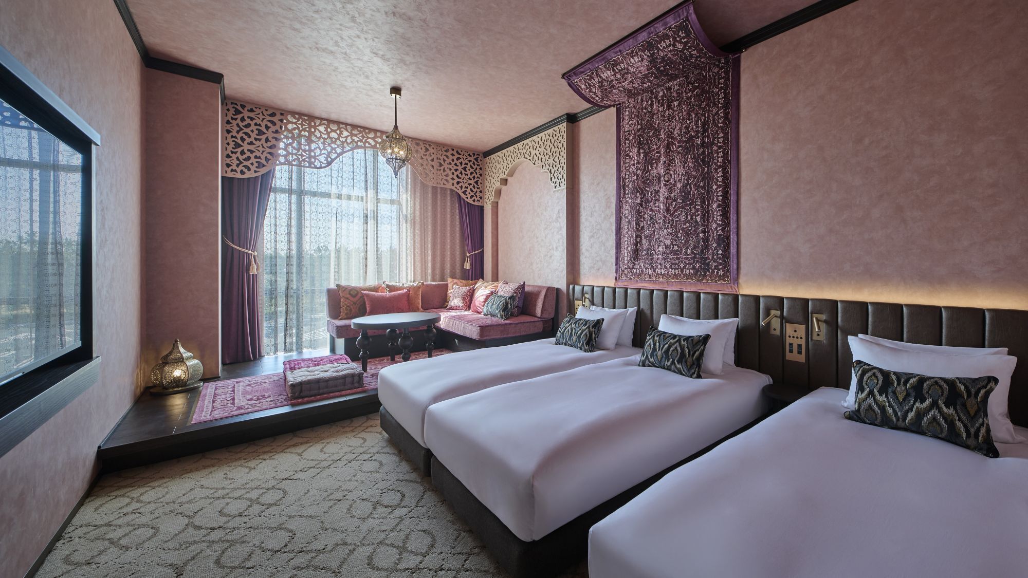 A hotel room with two beds, a sofa, a chandelier, and a large window with curtains.