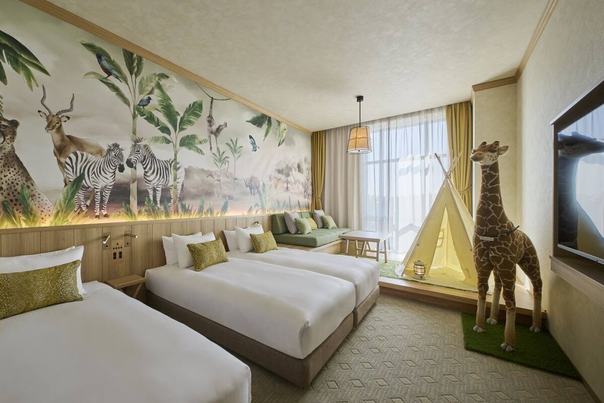 A hotel room with two beds, a mural of wildlife, a giraffe statue, a tent, and a large window.