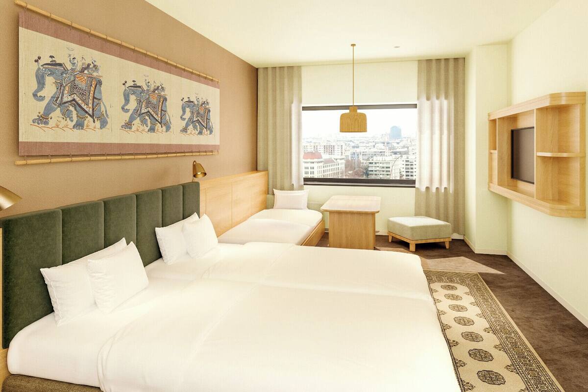 A hotel room with a large bed, a smaller bed, a desk, a TV, a window with a city view, and a decorative tapestry.