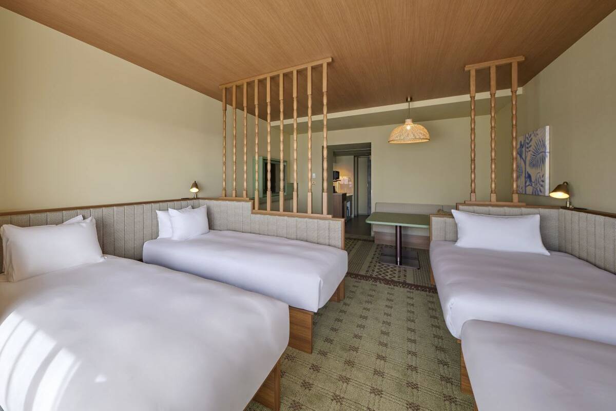A hotel room with three beds, a small table, and a hanging light fixture.