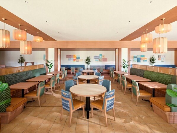 A spacious dining area with multiple seating options including booths and round tables, wooden flooring, and hanging pendant lights.