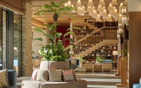 A modern interior with a staircase, a seating area with a plant, and a bookshelf.