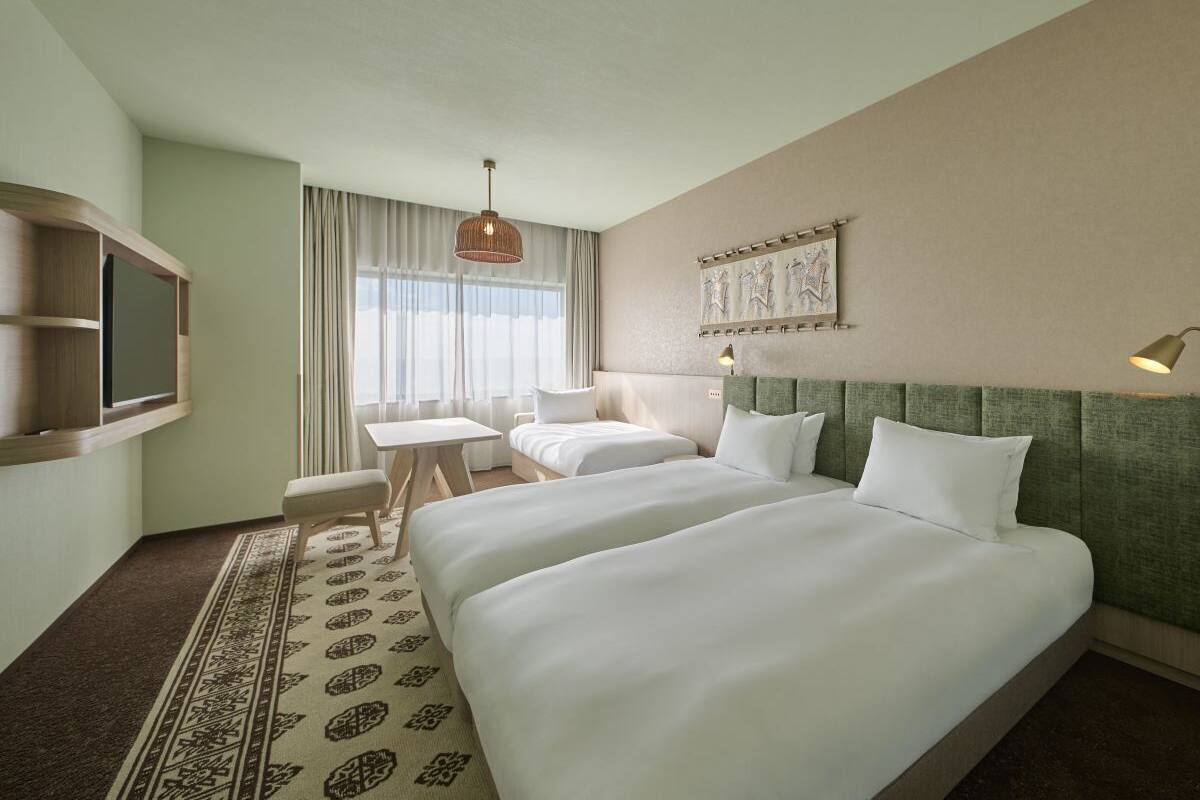A hotel room with two beds, a desk, a chair, a television, and a window with curtains.